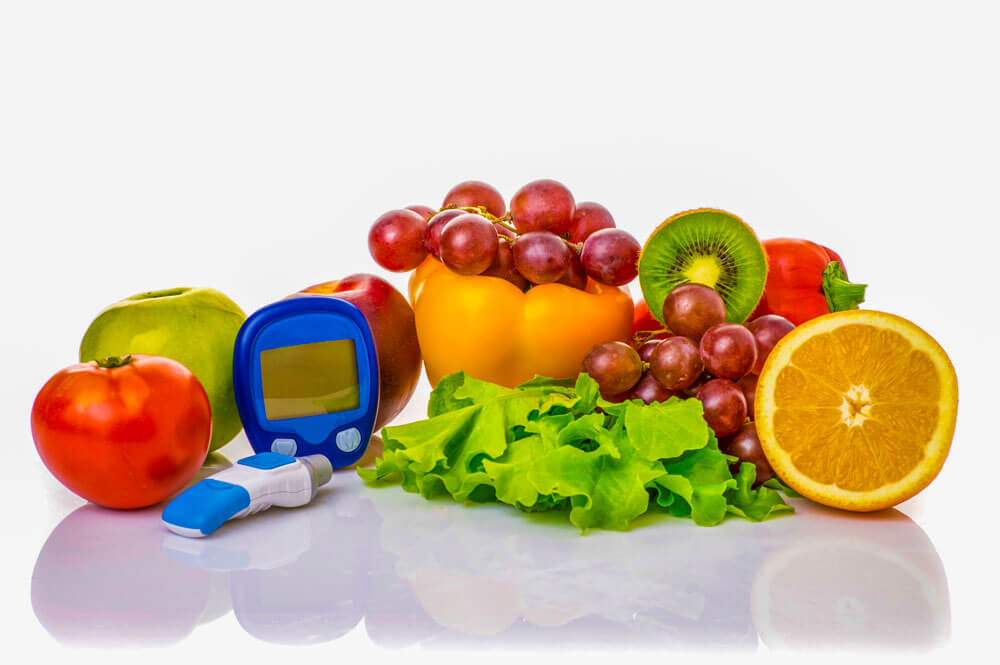 Fruits, vegetables, and diabetes monitors laying on a white table