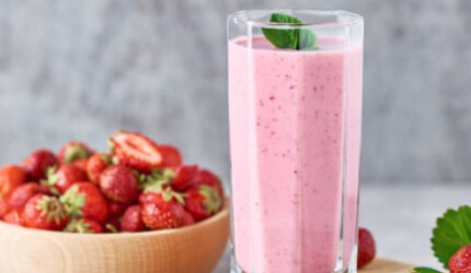A pink strawberry smoothie next to a bowl of strawberries