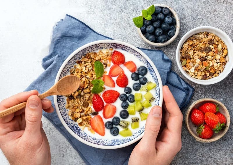 a persona eating a healthy fruit yogurt parfait