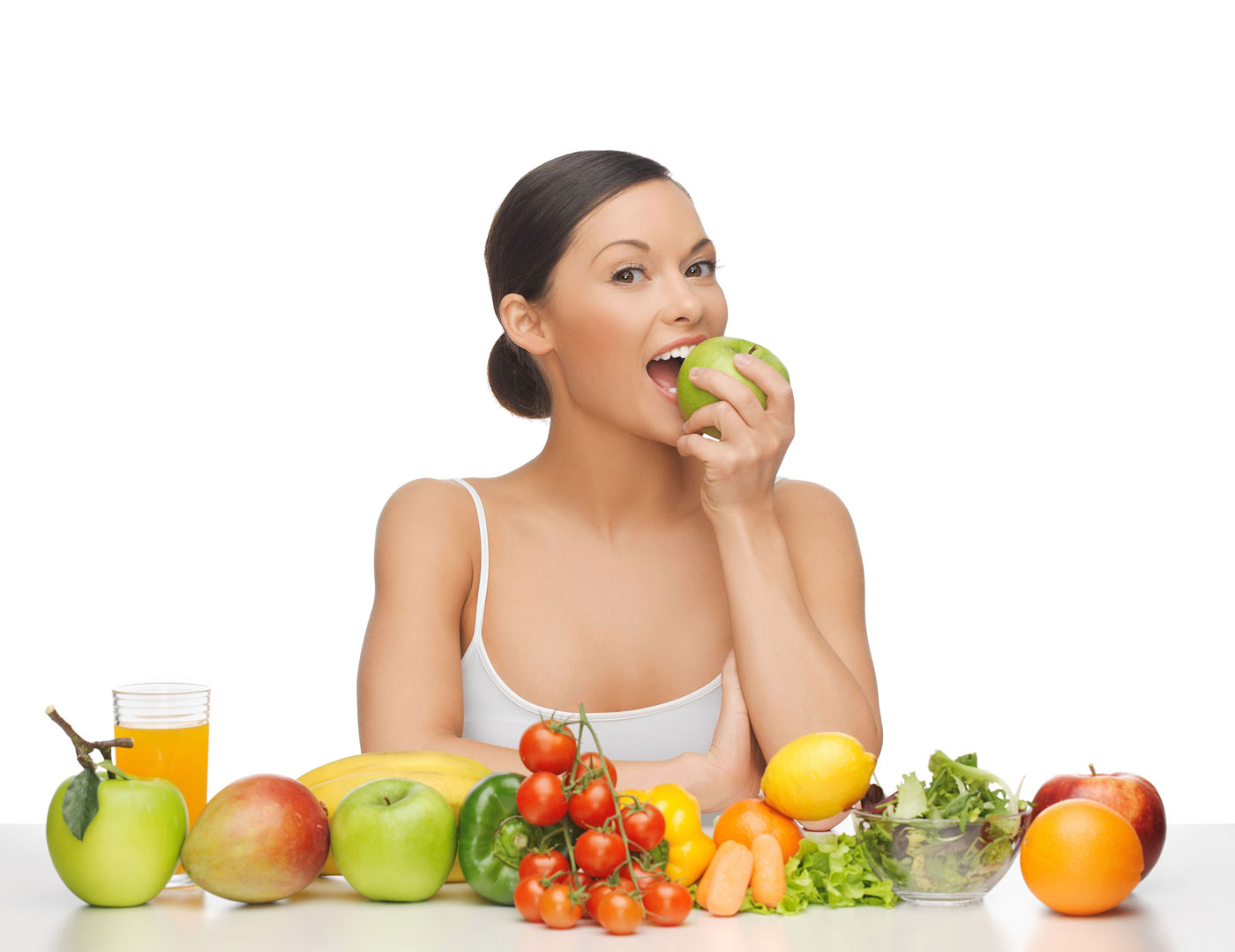 a woman eating an apple with fruits and vegetables in front of her.